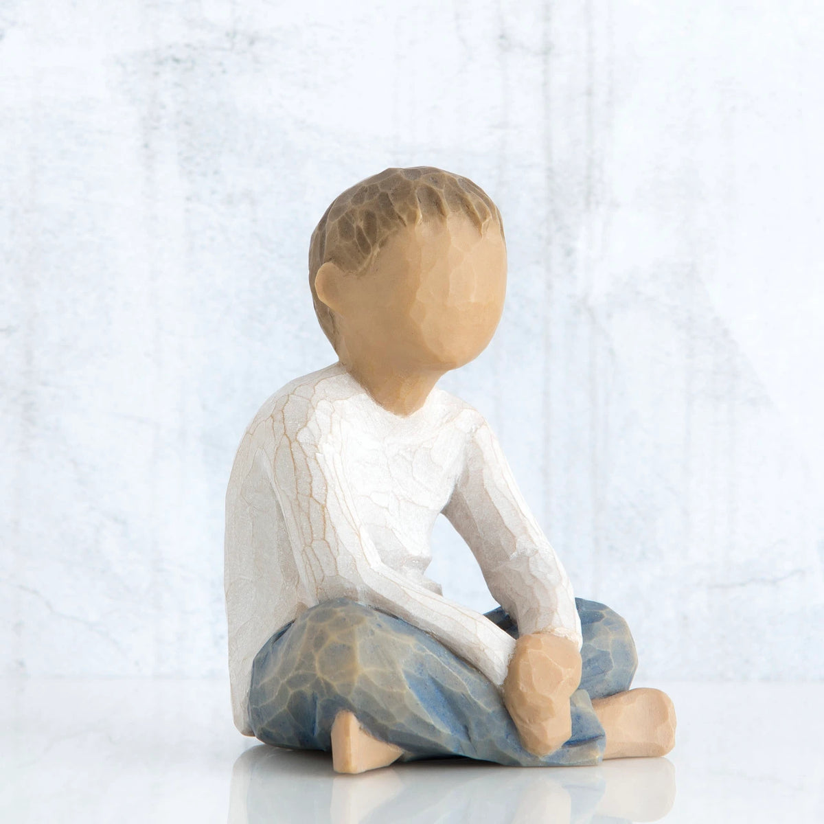 Small little boy figurine sitting down faceless, wearing white shirt and blue jeans