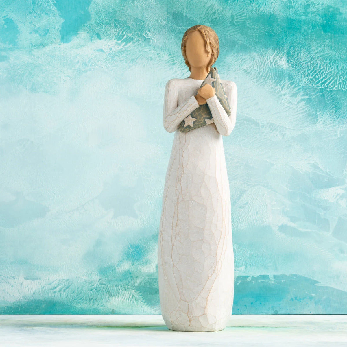 Willow Tree Hero, 9.5”h hand-painted standing resin figure in cream dress holding folded American flag in her arms, in front of aqua painting