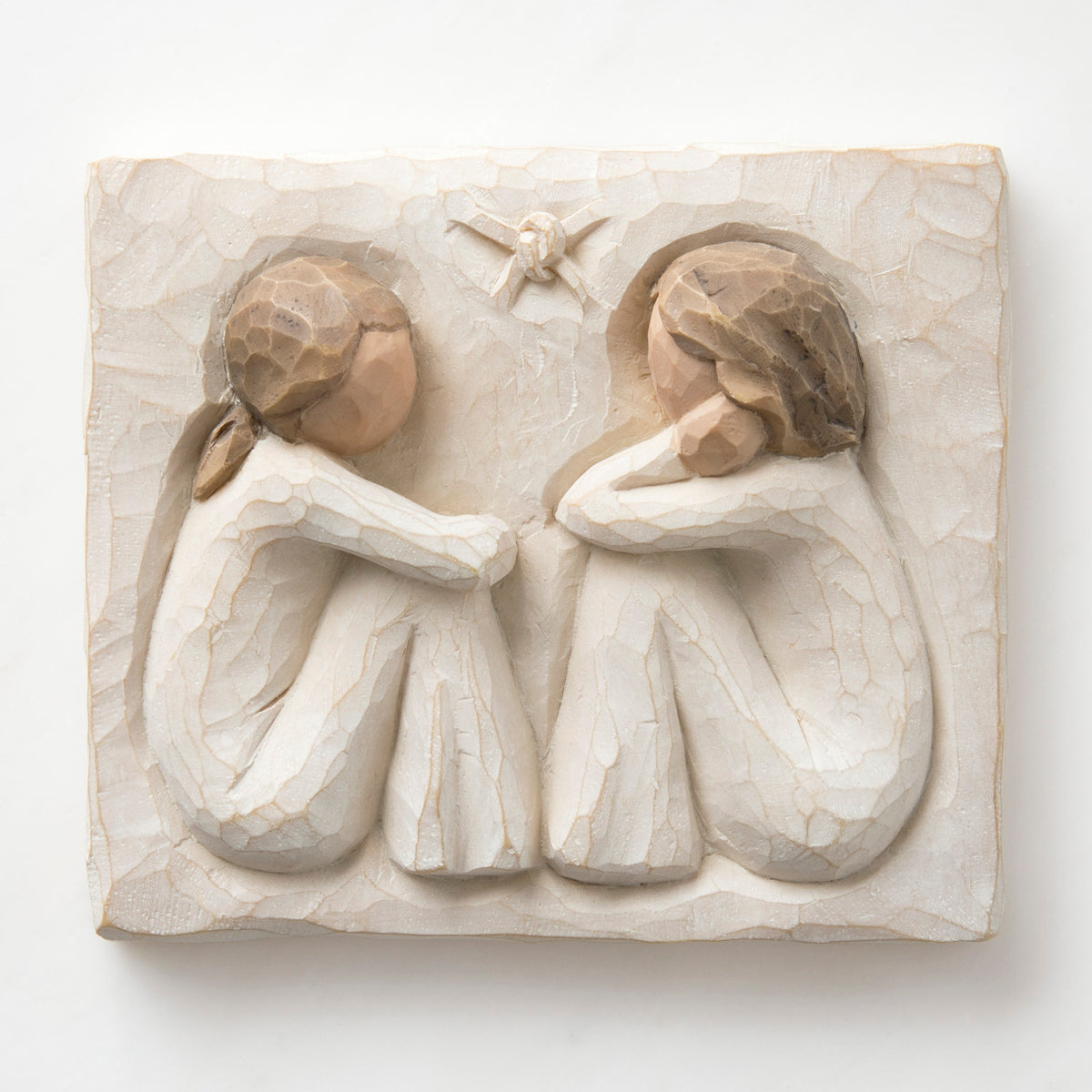 Close up white square carving - two faceless girls sitting looking at eachother wearing white dresses