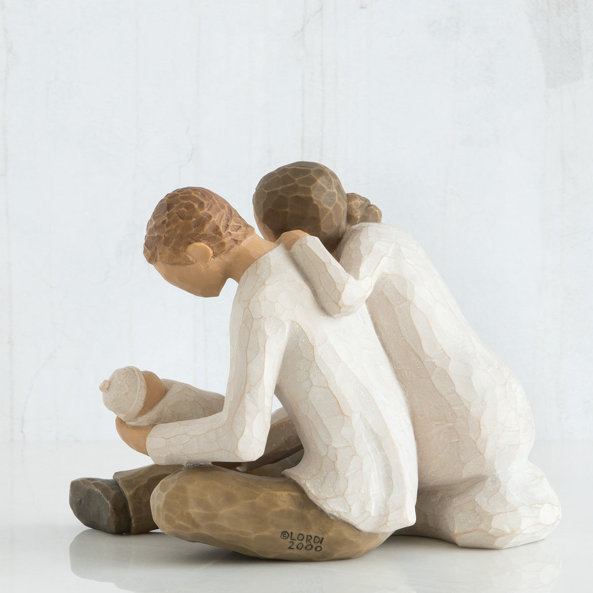 Man and woman couple figurines in white sitting down holding swaddled baby