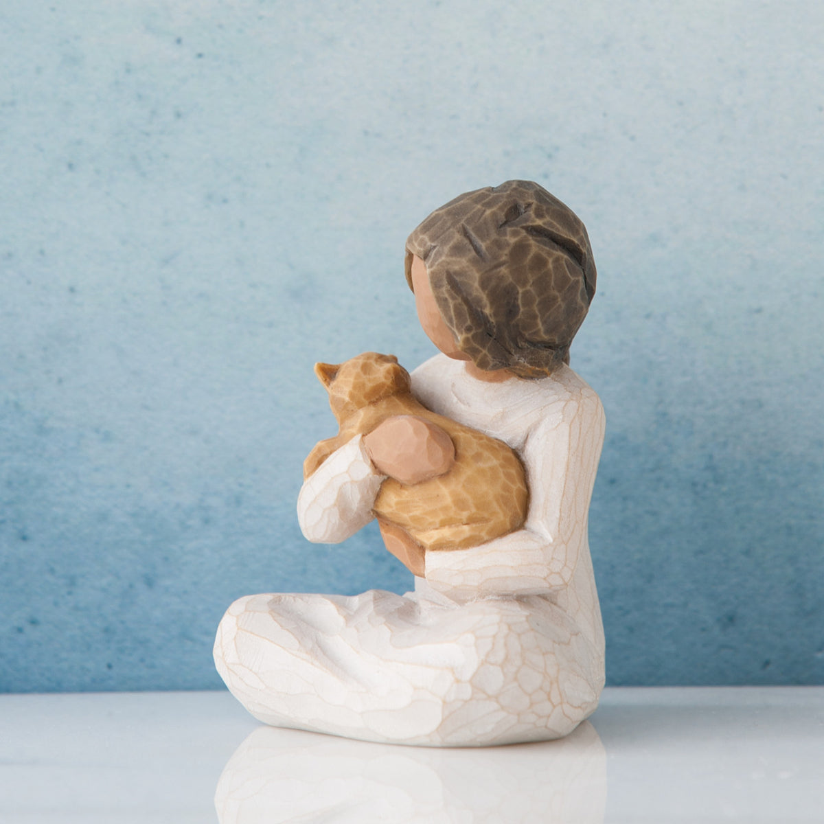 Small brunette girl figurine sitting wearing white dress holding golden cat figurine - blue background