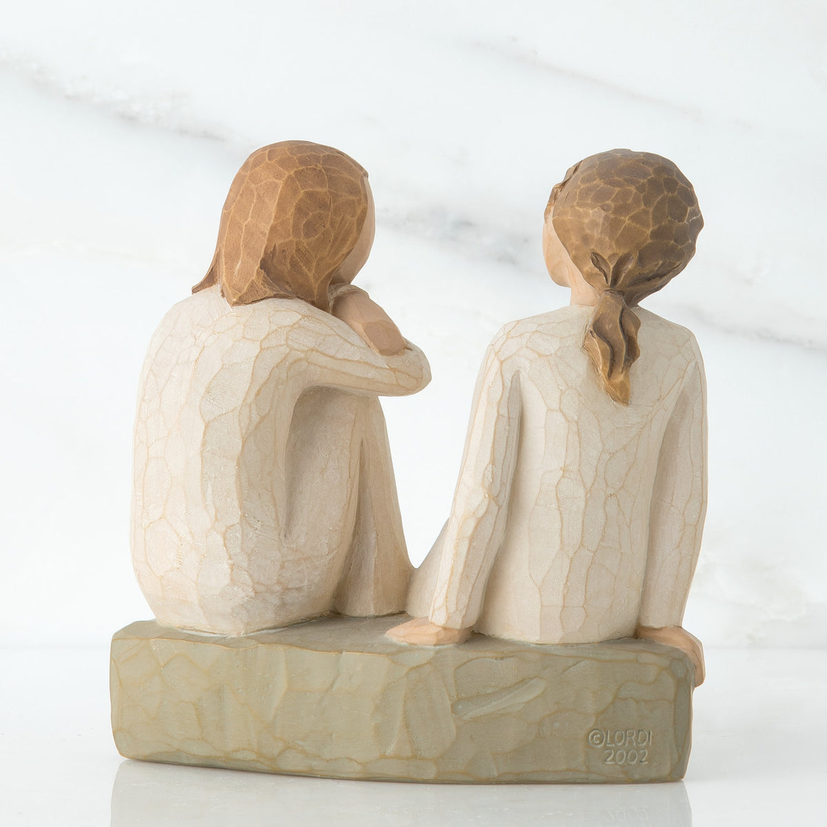 Back view of two brunette girl figurines in white sitting on a grey rock