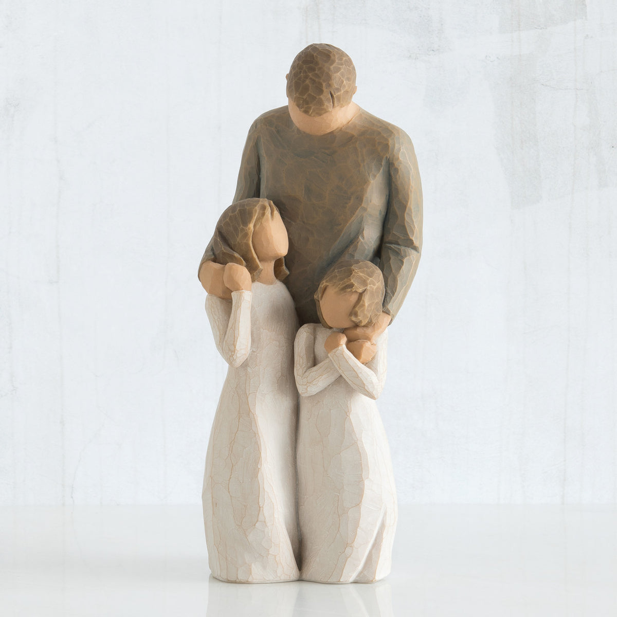 Man faceless figurine wearing brown shirt standing over two faceless girl figurines in white dresses