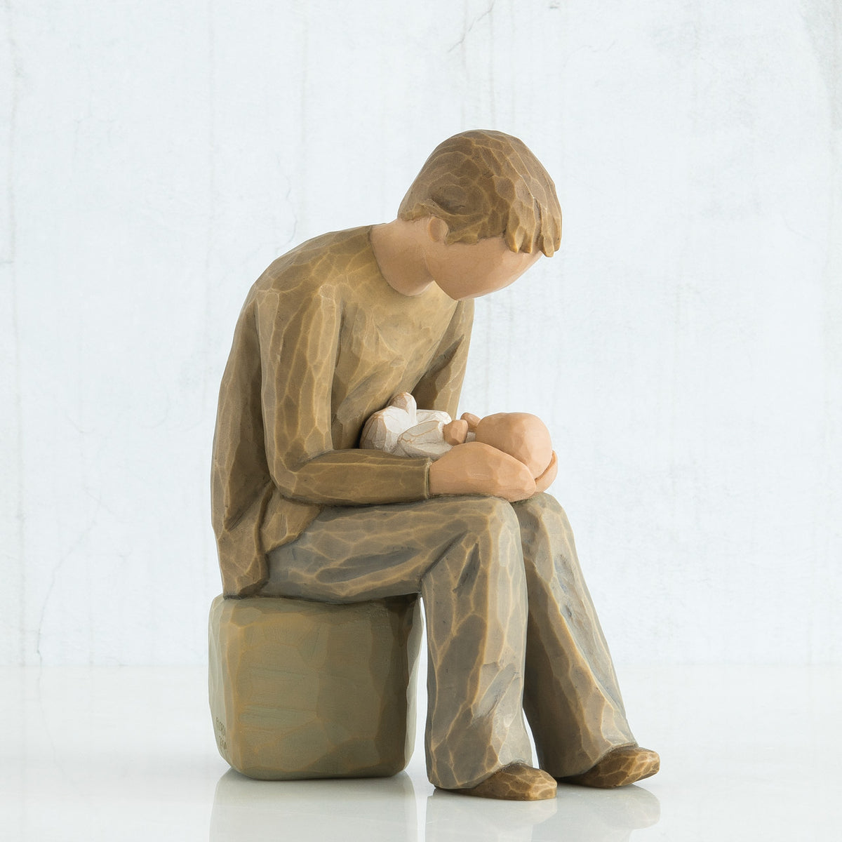 Man faceless figurine dressed in light brown sitting on rock holding baby in arms