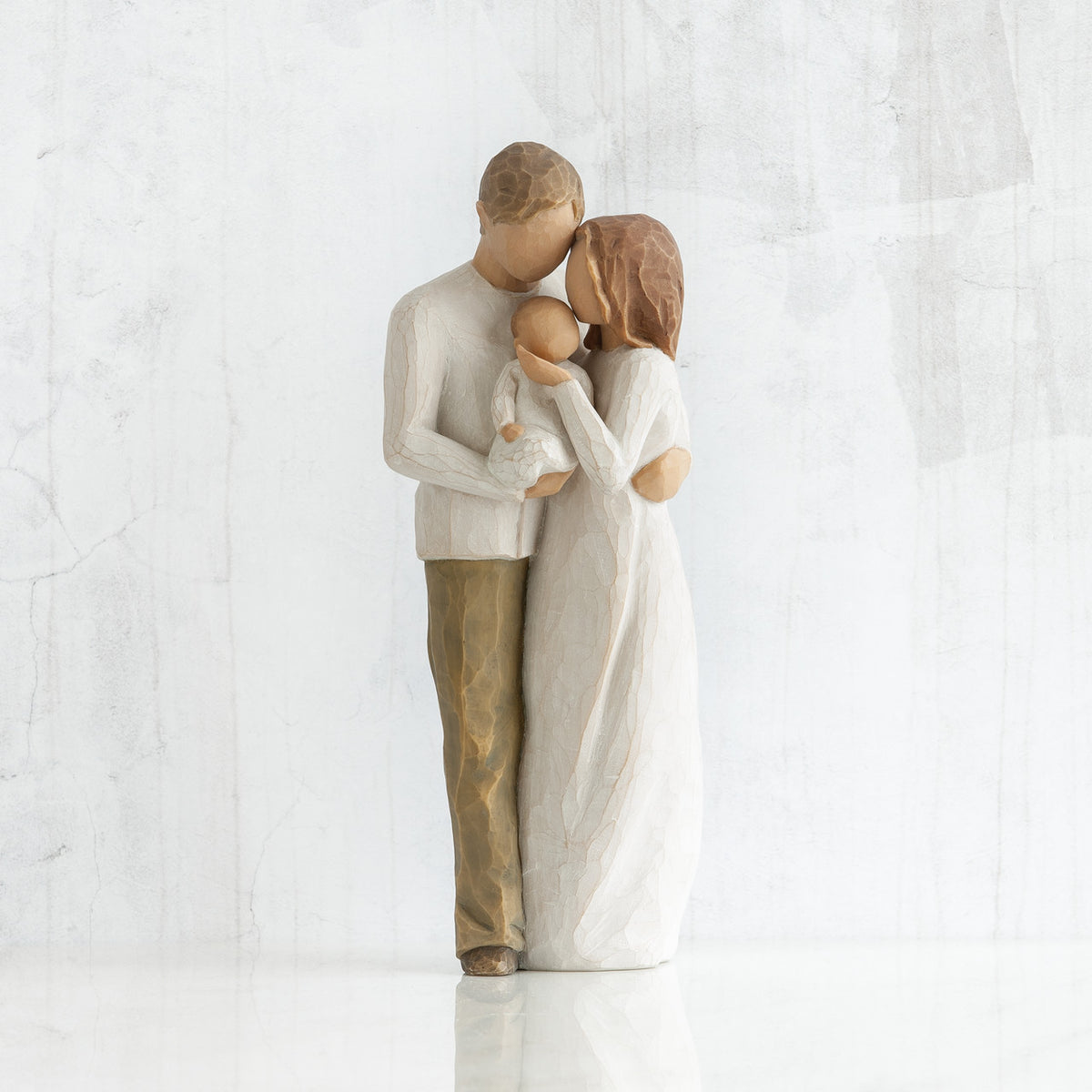 Faceless woman and man figurine standing holding baby in their arms - all in white