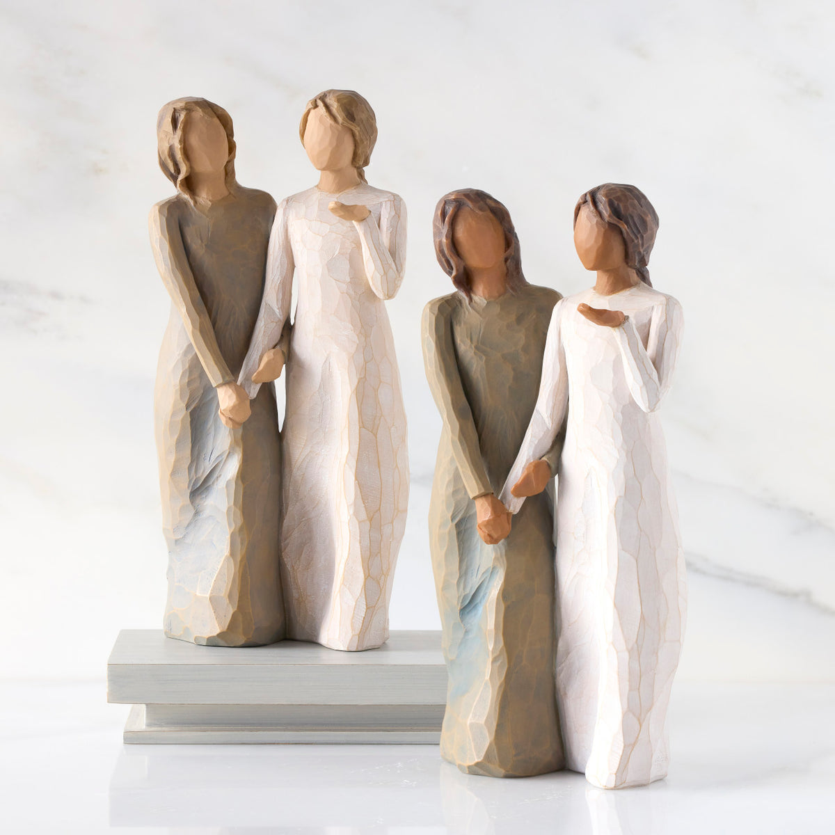 Lighter & Darker skin versions of two standing female figures, one in cream dress, one in blue-gray dress, holding hands and turned as if speaking to each other