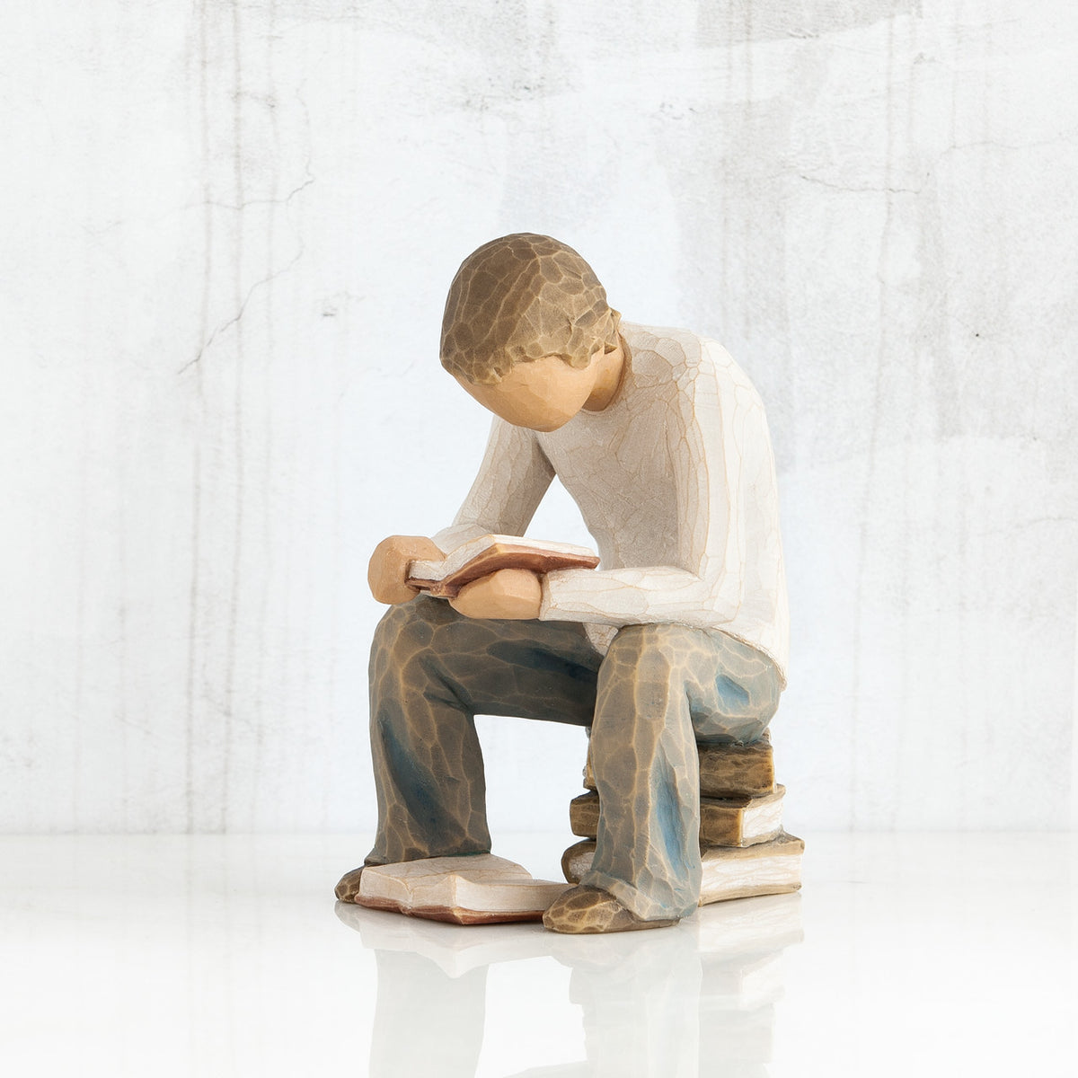 Young faceless boy figurine sitting on books with book opened in his hands - another book on the floor of his feet