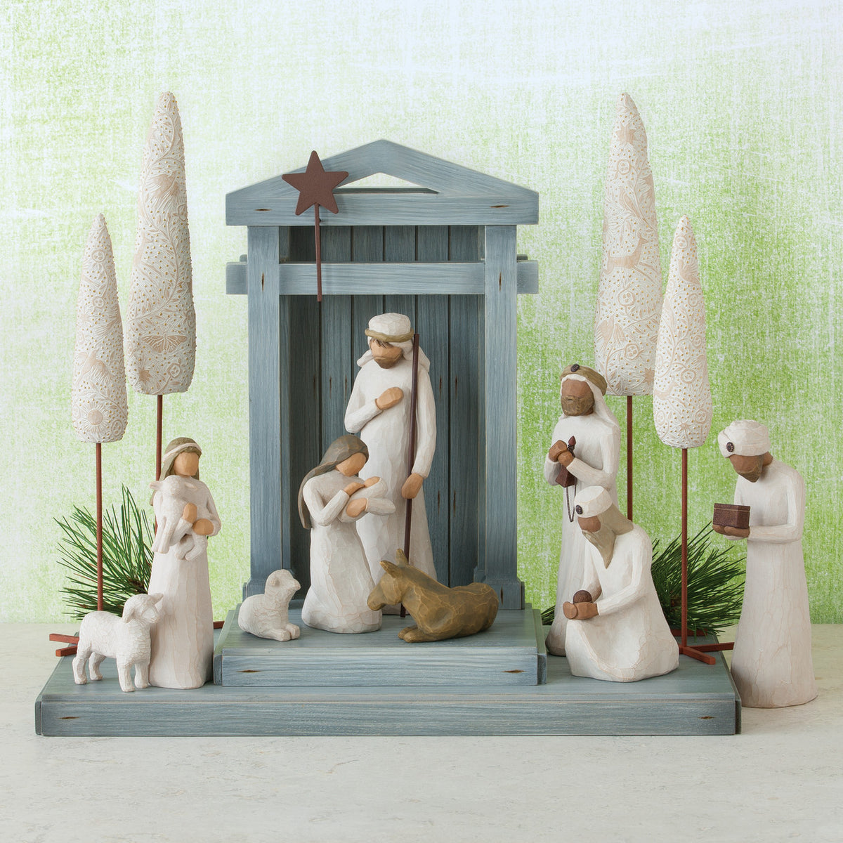 Front view of light grey barn figurine with several wiseman in white around it and four large white trees - light green background