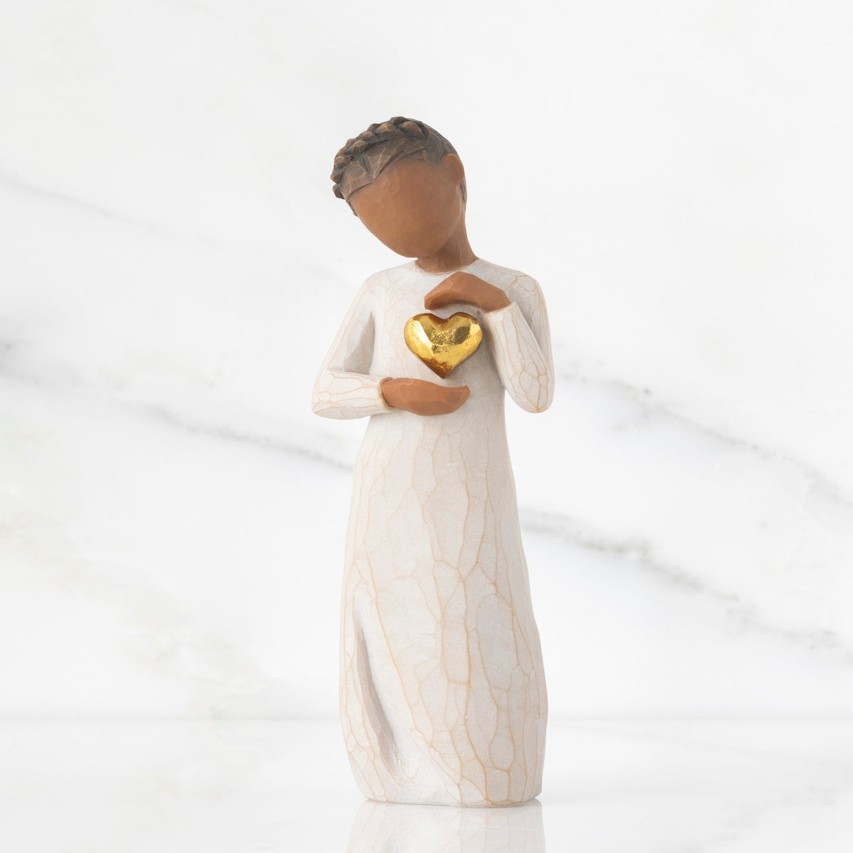 Front view: standing figure in cream dress with darker skin and dark hair braid, framing gold leaf heart with both hands on chest