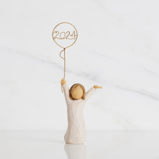Front view: standing figure in cream dress, arms raised, holding gold wire balloon with 2024 written in gold wire inside