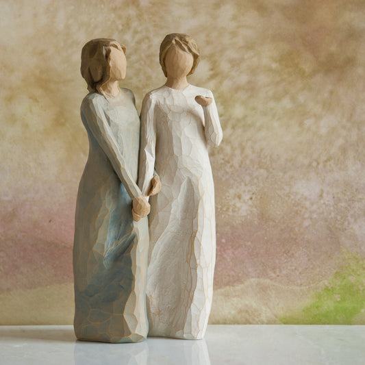 Willow Tree My sister, my friend, 8.5”h hand-painted figure of two females standing next to each other, arms/hands connected, one in cream dress, one in blue/gray dress, in front of dusty pink painting