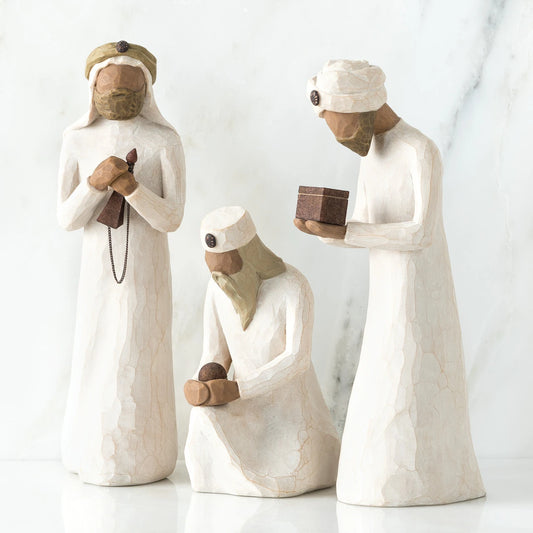Set of three wiseman figurines -two are standing - far right one standing is holding brown box - one is sitting in the middle holding a rock
