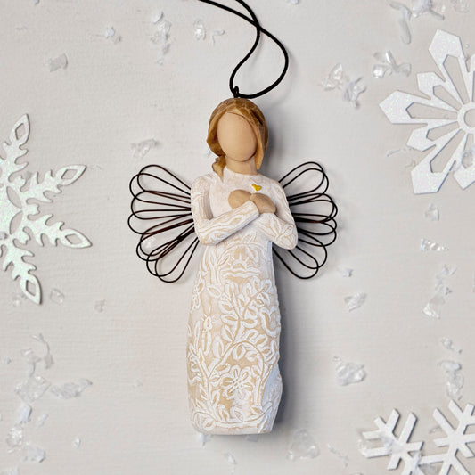 Willow Tree Remembrance Ornament, 4.5”h hand-painted resin angel figure in cream dress carved with symbols of nature, wire wings, crossed hands under small gold-leaf heart, brown elastic cord, laying amongst snowflakes