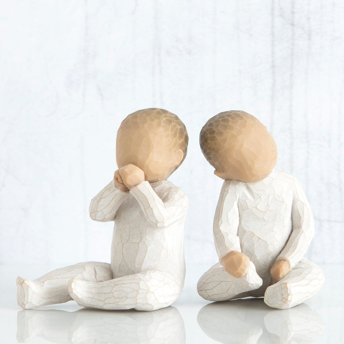 Set of two small baby figurines sitting in white facing each side