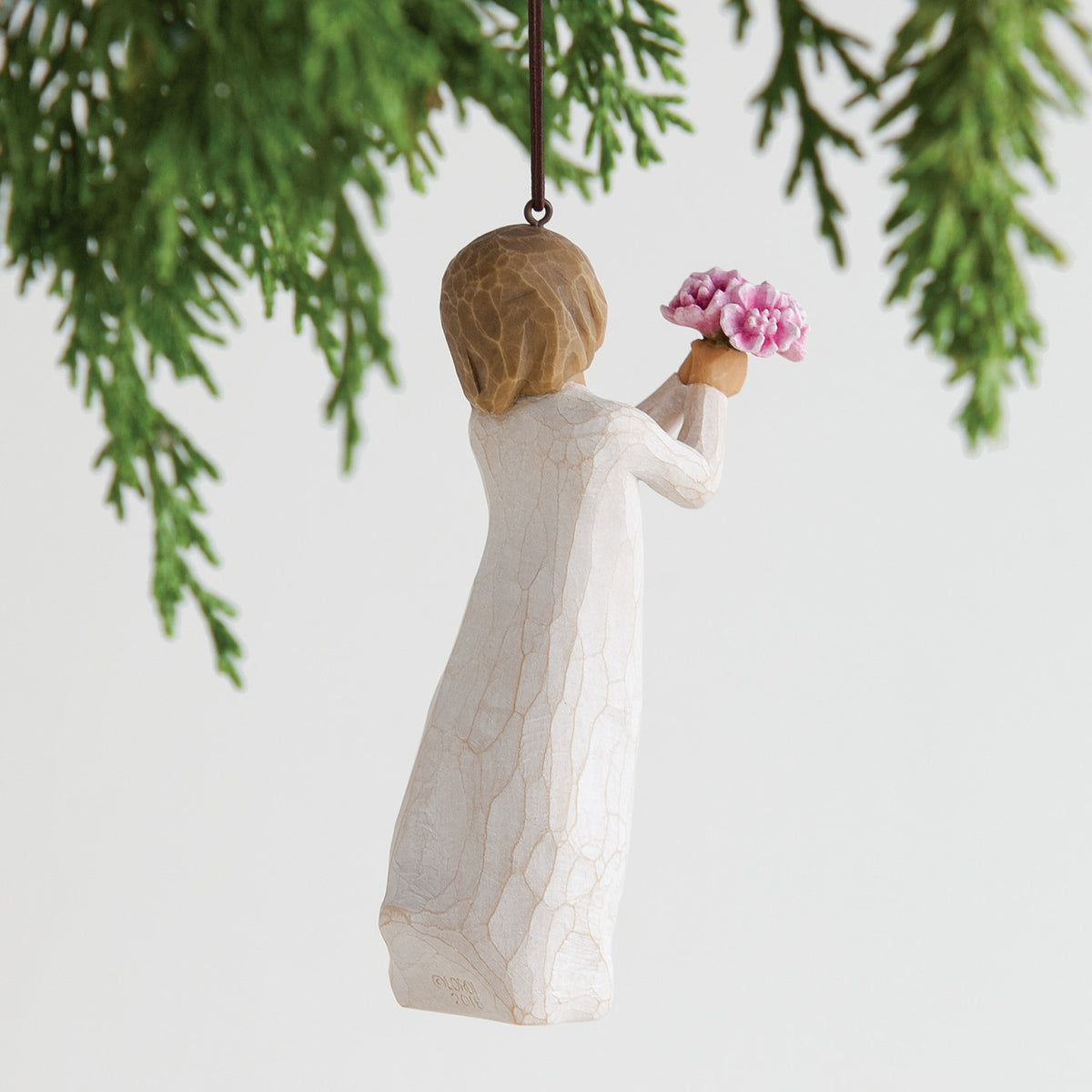 Back view of woman ornament with short brown hair, holding out a bouquet of pink flowers. Brown string attached to top of ornament