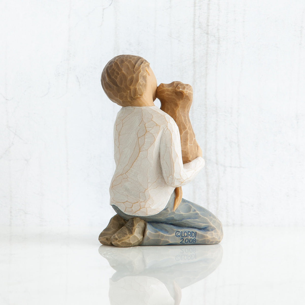 Back view of boy with light brown hair wearing white shirt and jeans and holding a light brown puppy as it licks his face.
