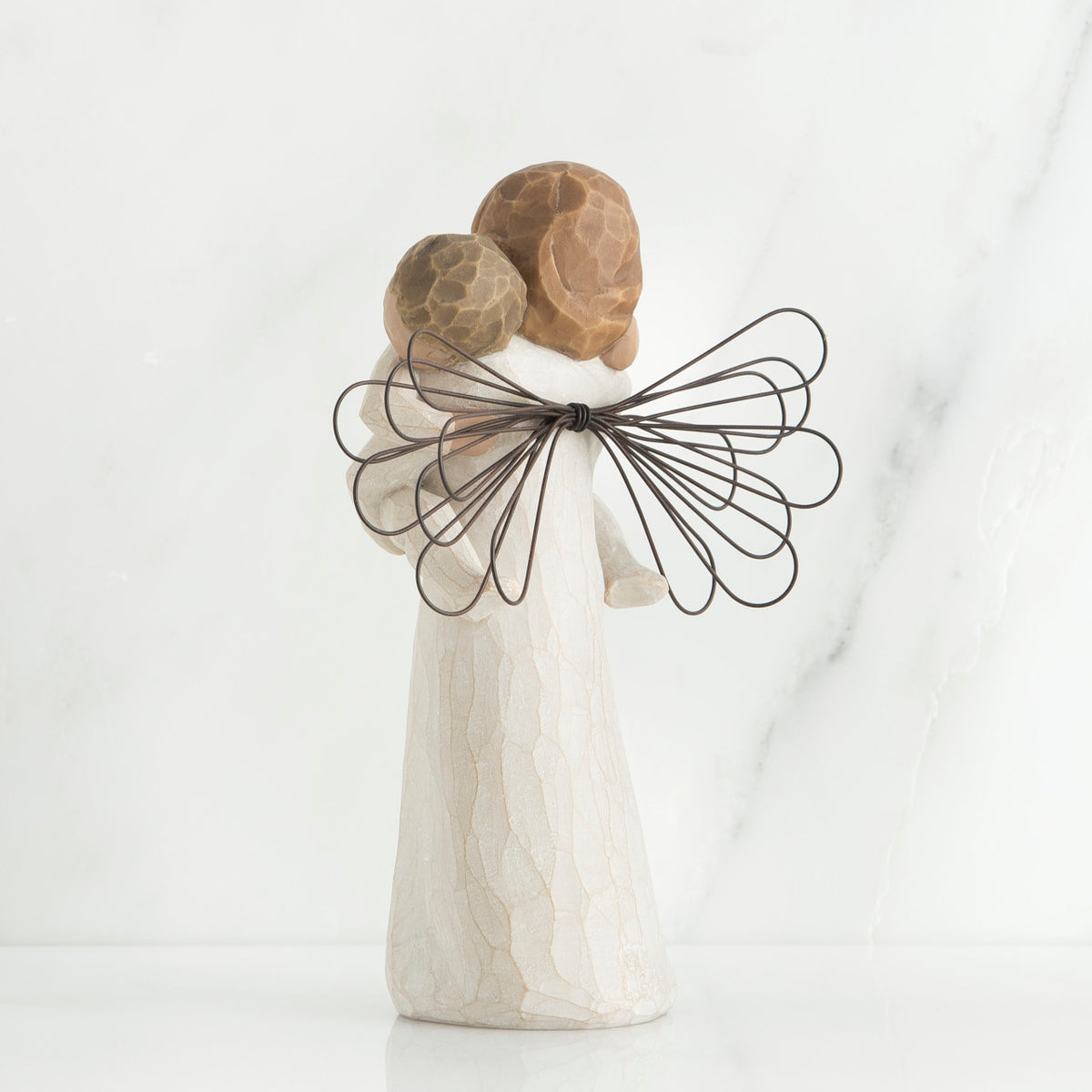 Back view of brunette girl figurine in white dress with brown wings holding baby
