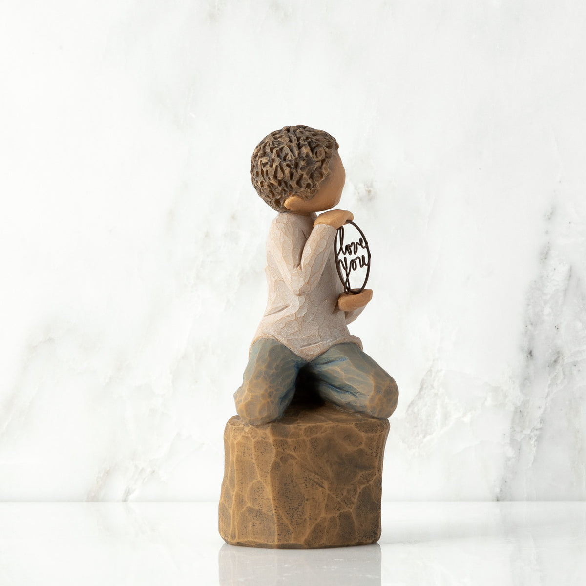 Right view: Figure of lighter-skin child, kneeling on rock, holding wire circle with ‘love you’ written in wire