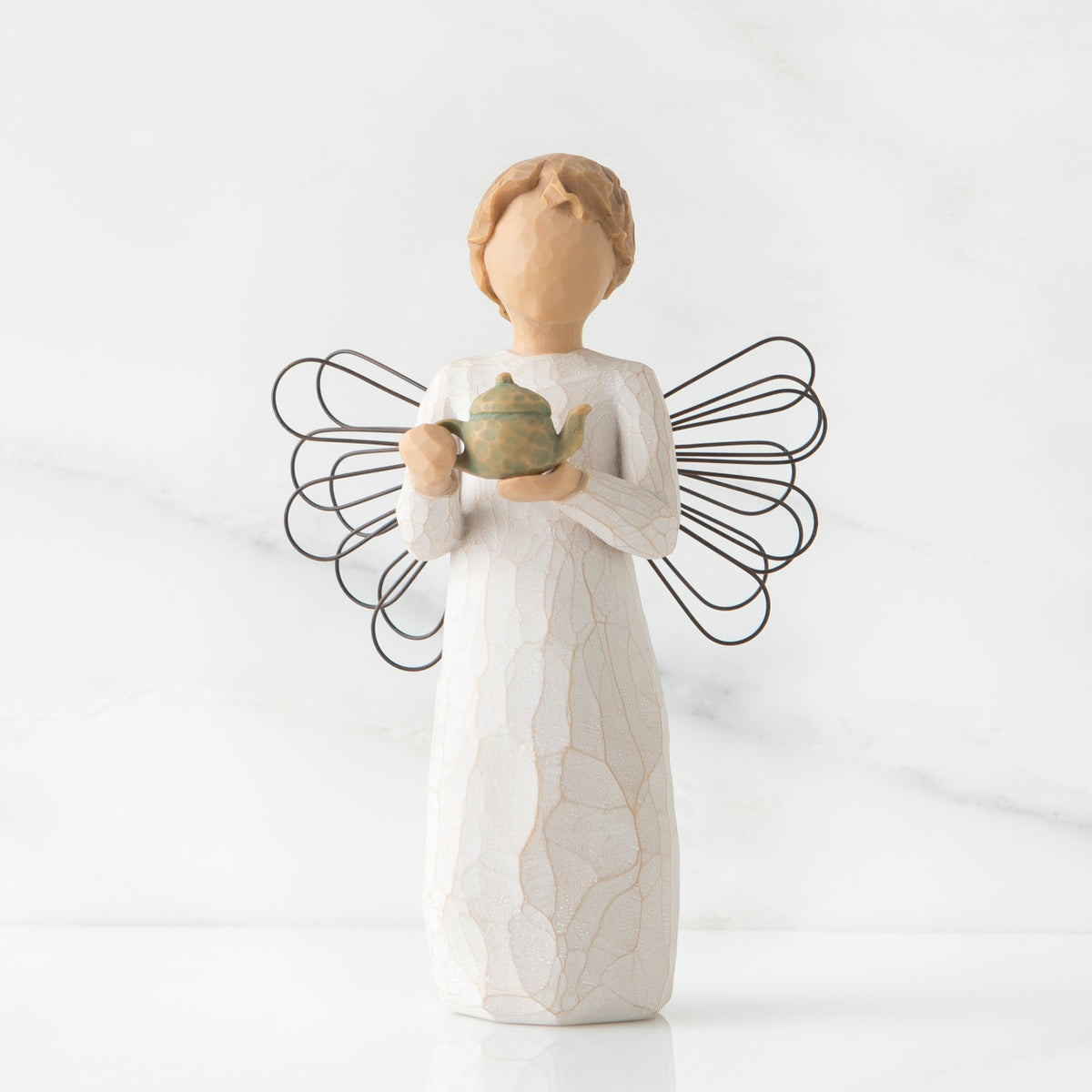 Faceless angel figurine with black wire wings dressed in white holding teapot
