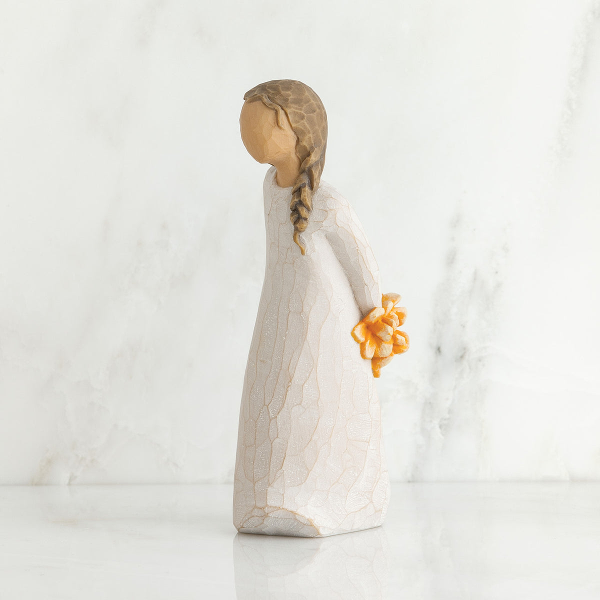 Right side view of girl with brown hair in braid over right shoulder leaning forward as she holds orange flowers behind her back