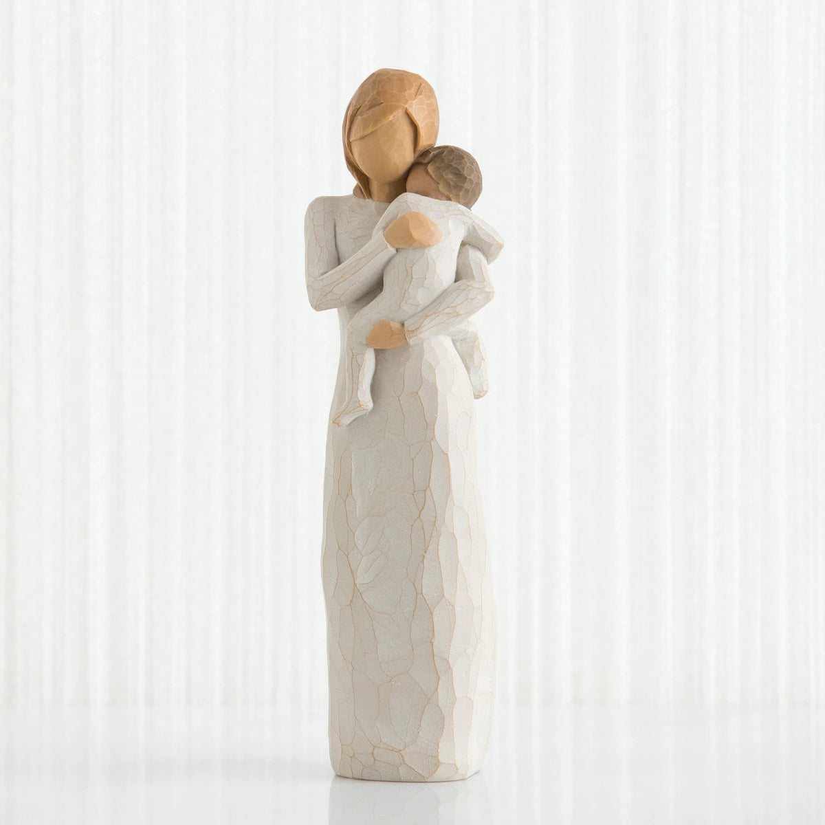 Faceless woman figurine in white dress holding brown haired baby in white clothes